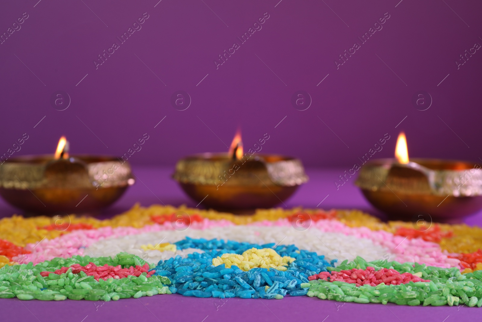 Photo of Diwali celebration. Diya lamps and colorful rangoli on purple background, closeup