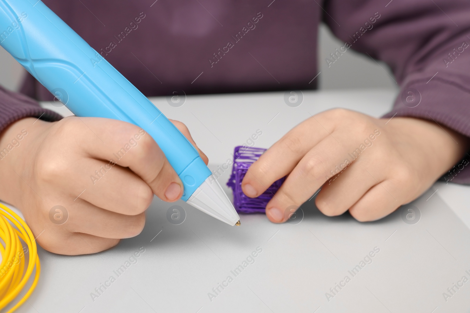 Photo of Boy drawing with stylish 3D pen at white table, closeup