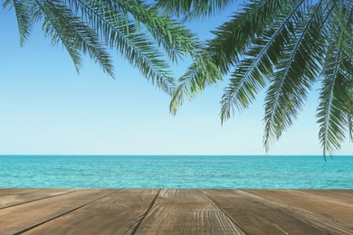 Image of Wooden table under green palm leaves near ocean