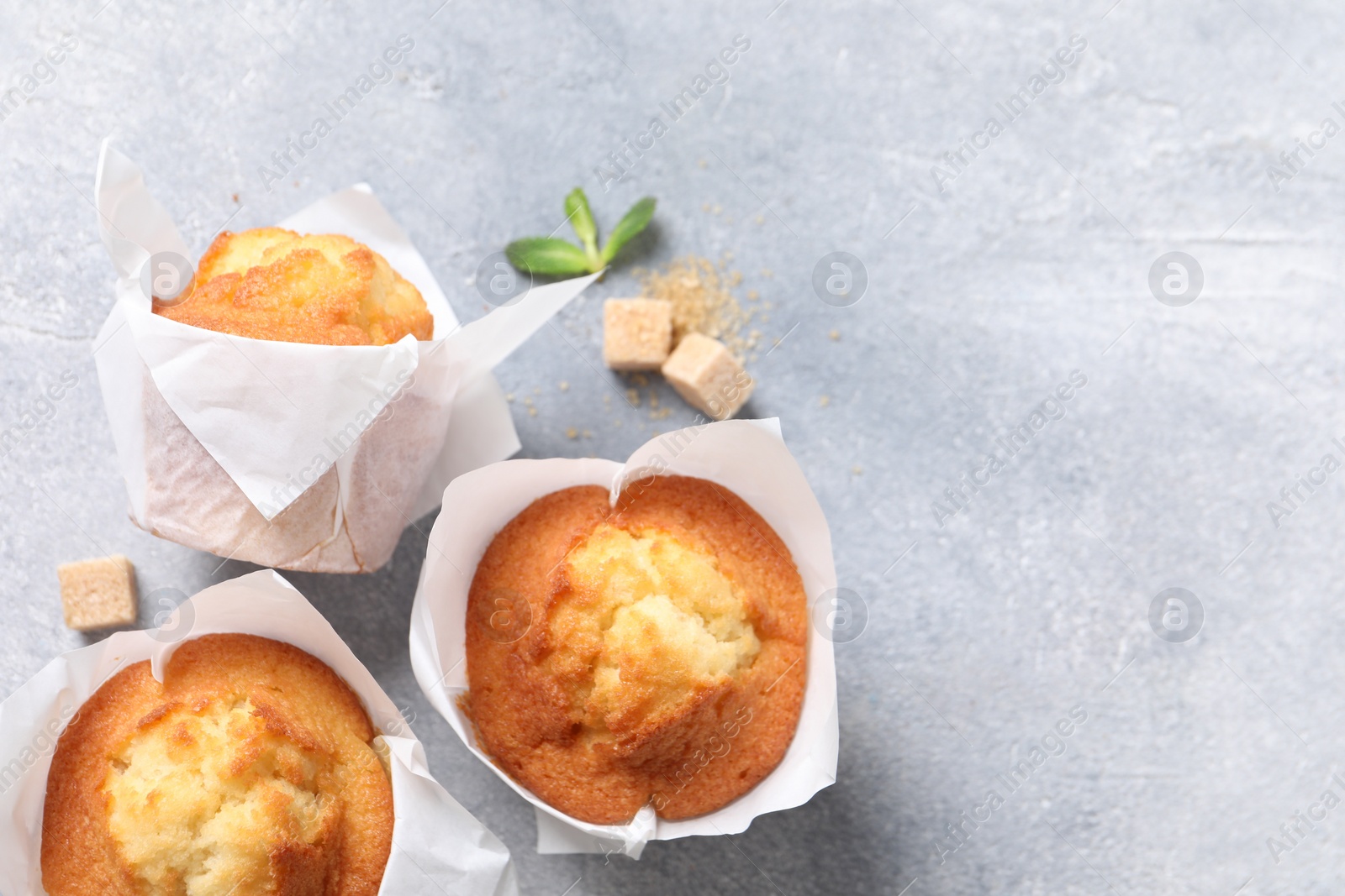 Photo of Delicious sweet muffins and brown sugar on light grey textured table, flat lay. Space for text