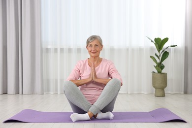 Photo of Happy senior woman practicing yoga on mat at home