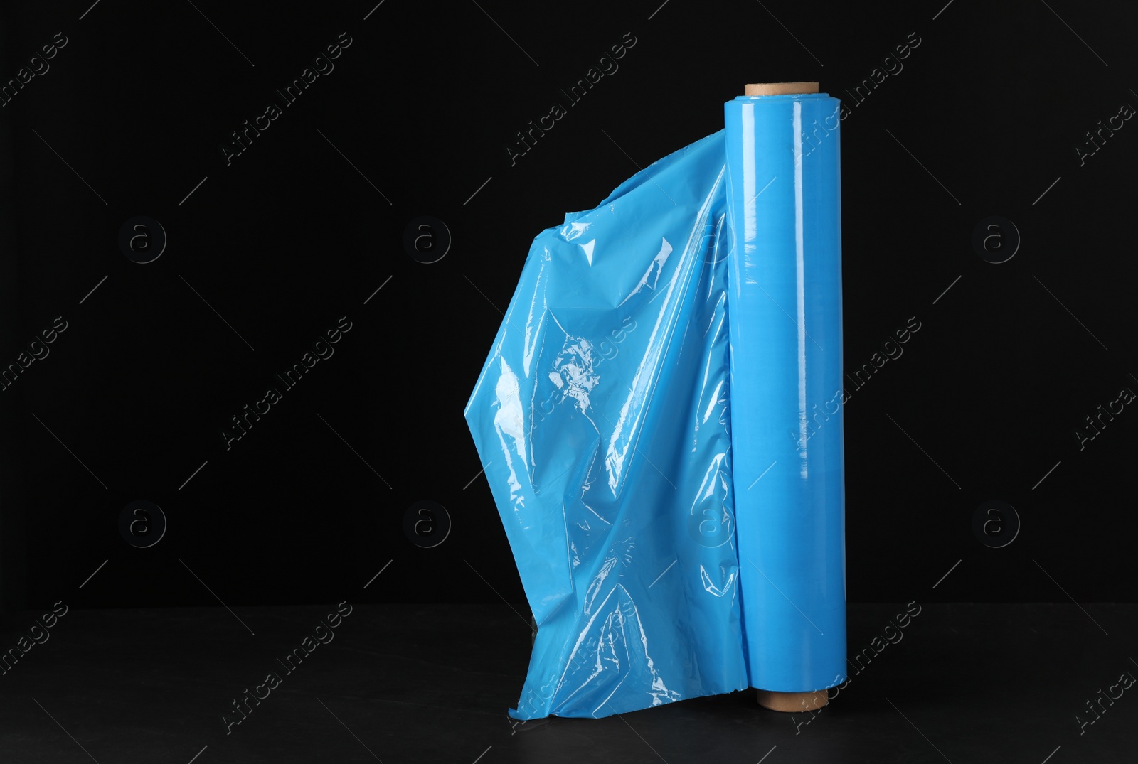 Photo of Roll of plastic stretch wrap film on table against black background, space for text