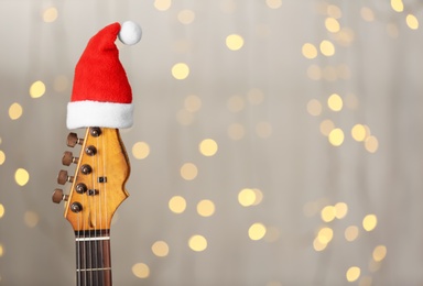 Photo of Guitar with Santa hat against blurred lights, space for text. Christmas music