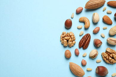 Different delicious nuts on light blue background, flat lay. Space for text