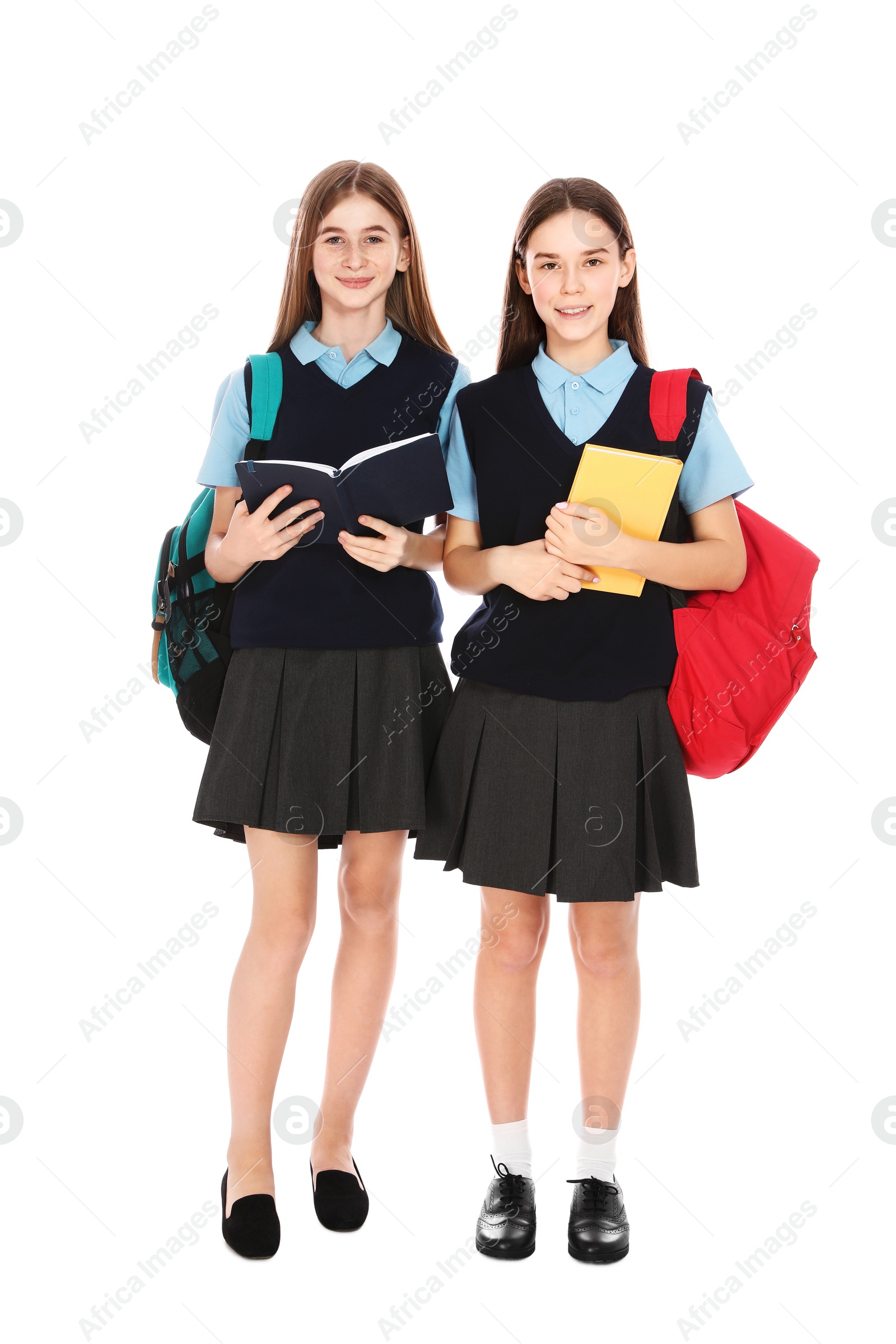 Photo of Full length portrait of teenage girls in school uniform with backpacks and books on white background