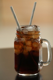 Mason jar of cola with ice on table against blurred background