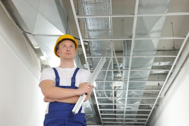 Worker with metal profile indoors. Suspended ceiling installation