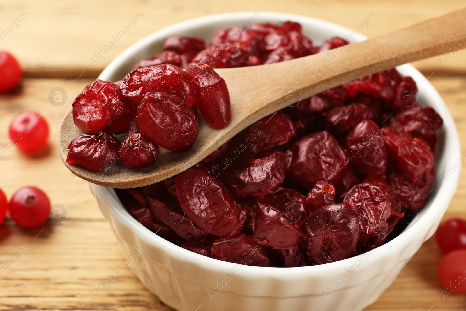 Photo of Tasty dried cranberries in bowl and fresh ones on wooden table, closeup