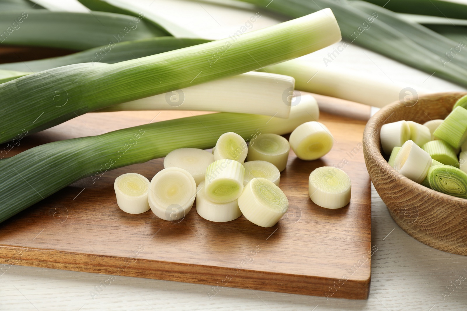 Photo of Whole and cut fresh leeks on white wooden table, closeup