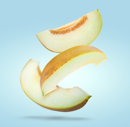 Image of Delicious ripe melon slices falling on pale light blue background