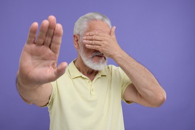 Photo of Embarrassed senior man covering face on purple background