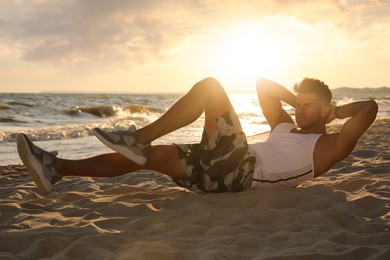Photo of Sporty man with athletic body doing crunches on beach