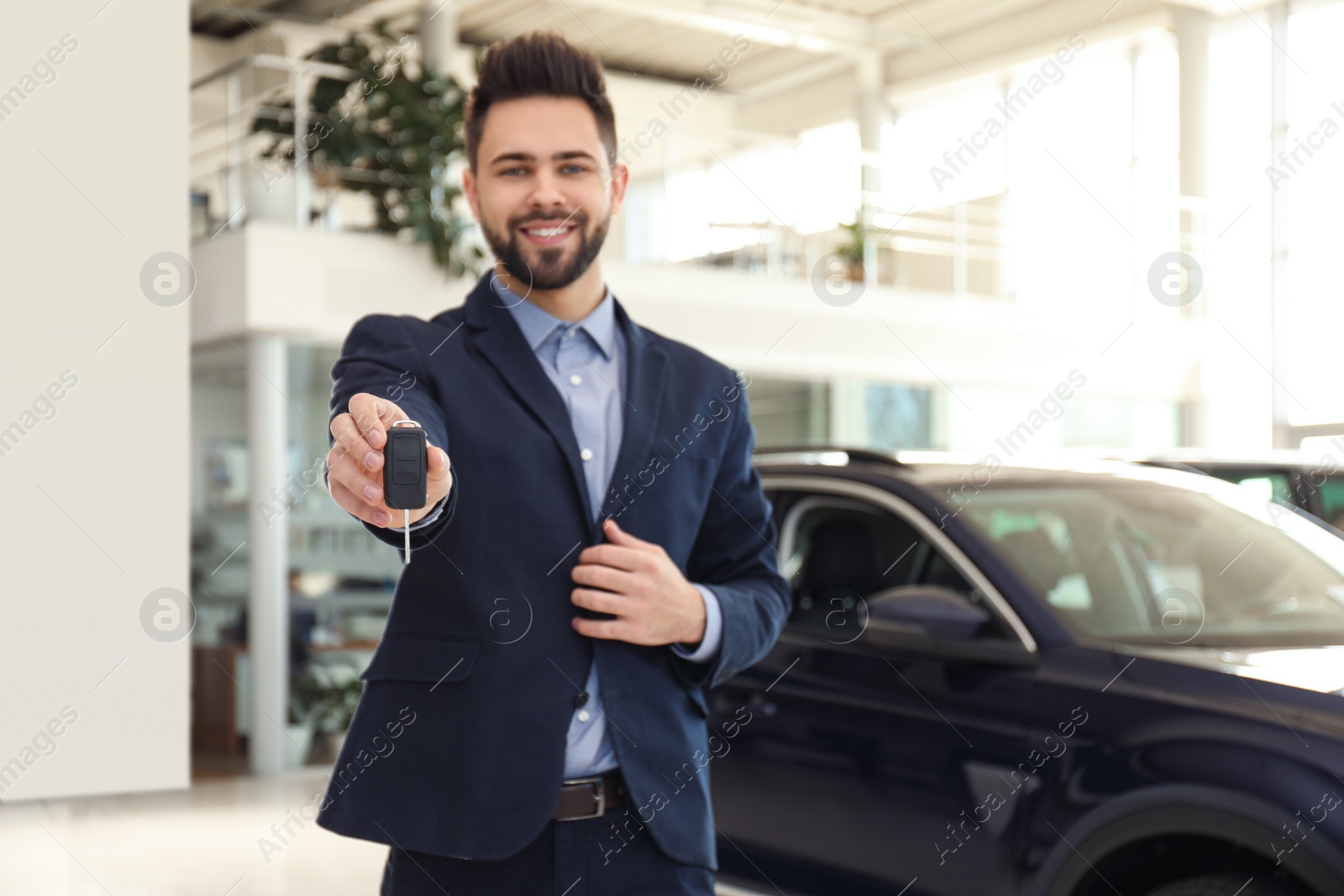 Photo of Salesman with key in modern car salon