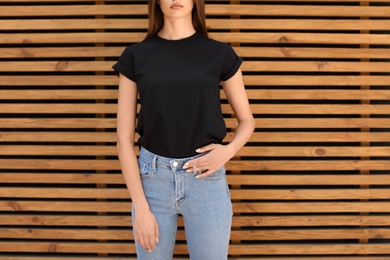 Photo of Young woman wearing black t-shirt against wooden wall on street. Urban style