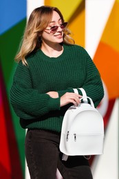 Young woman with stylish backpack near color wall