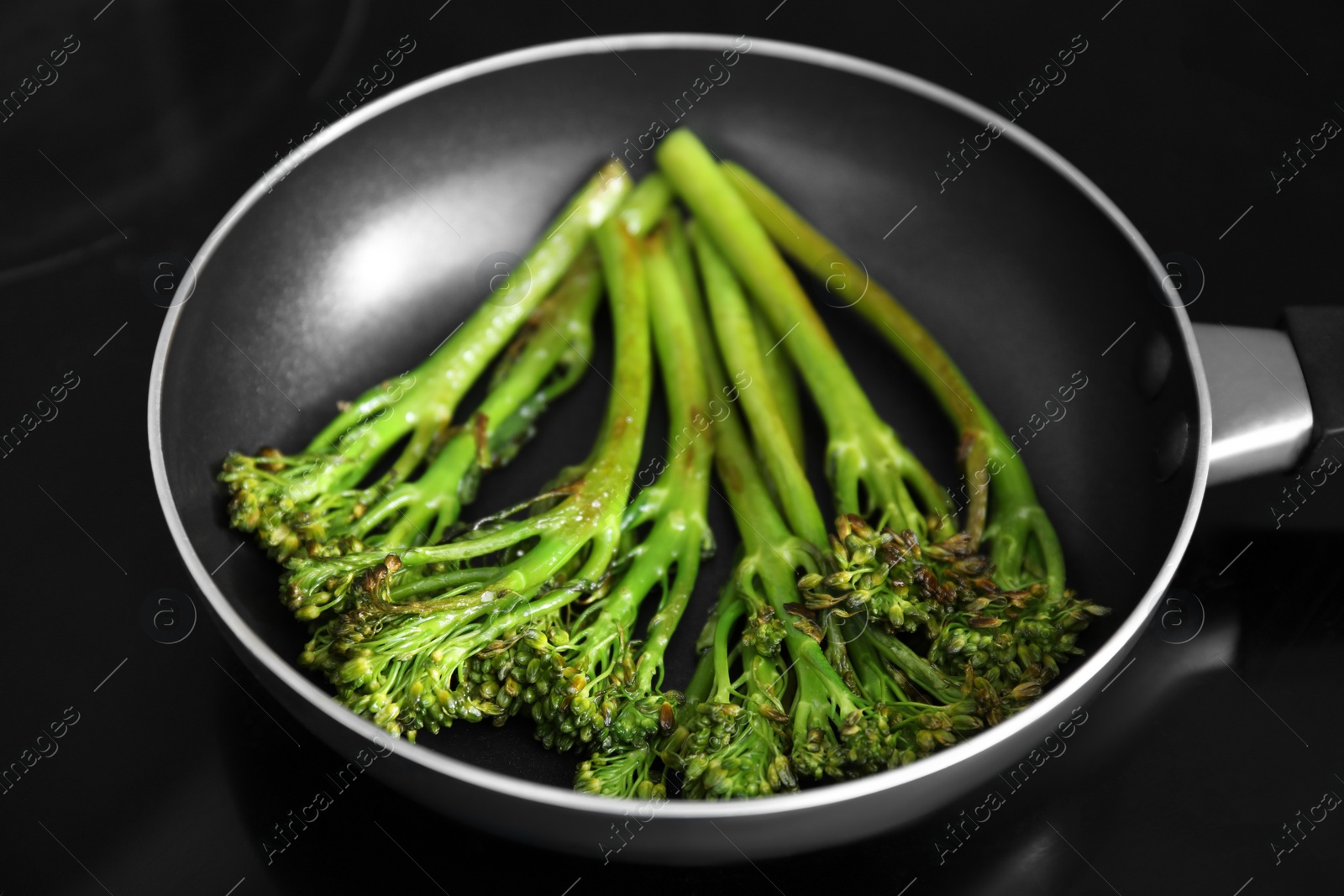 Photo of Frying pan with tasty cooked broccolini on cooktop, closeup