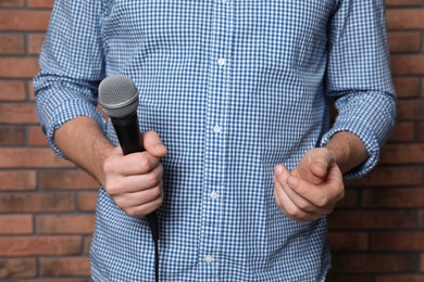 Photo of Man in shirt holding microphone near brick wall, closeup