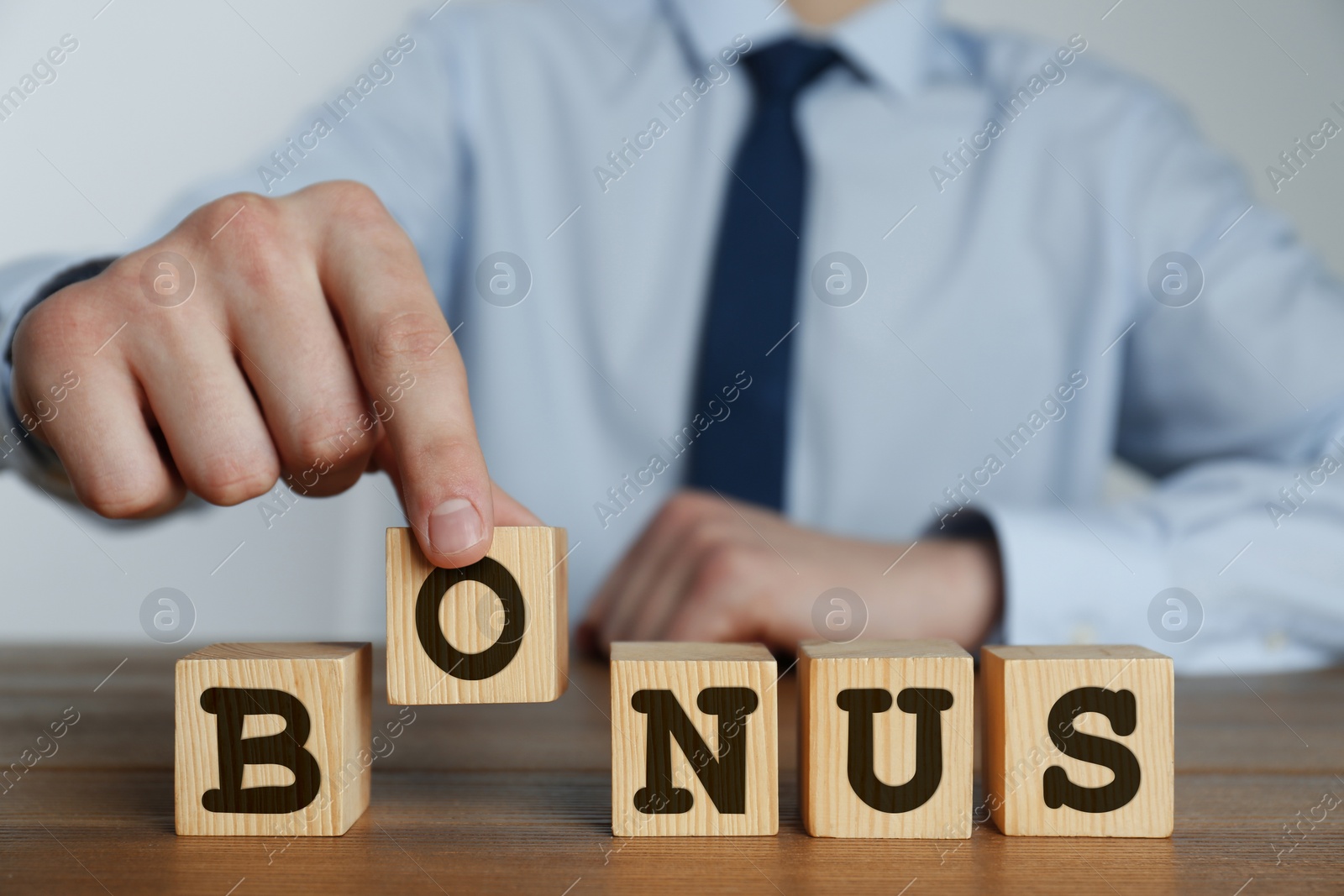 Image of Man making word Bonus of cubes with letters on wooden table, closeup