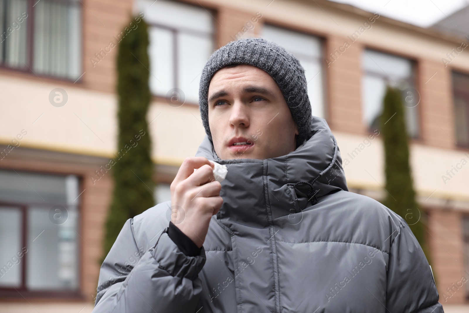 Photo of Sick young man with tissue on city street. Cold symptoms