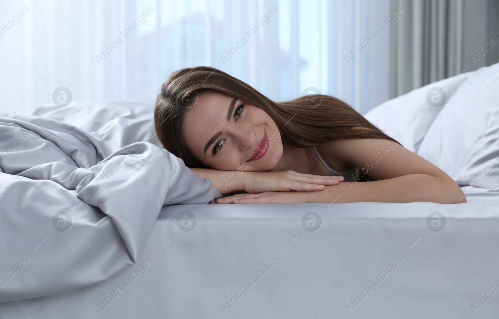 Photo of Young woman lying on comfortable bed with silky linens