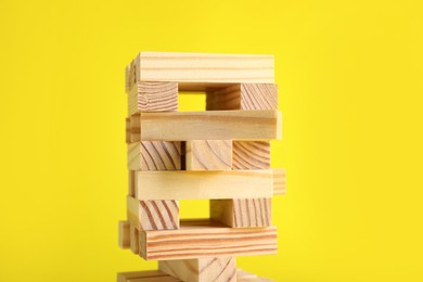 Photo of Jenga tower made of wooden blocks on yellow background, closeup