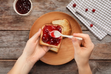 Photo of Woman spreading sweet jam on toast over table, top view