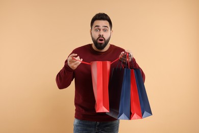 Photo of Shocked man with many paper shopping bags on beige background
