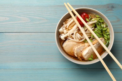 Photo of Delicious ramen with meat in bowl and chopsticks on light blue wooden table, top view. Space for text