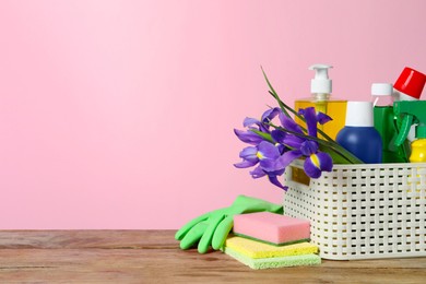 Spring cleaning. Basket with detergents, flowers and sponges on wooden table against pink background. Space for text