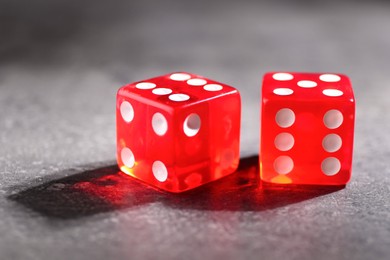 Two red game dices on grey textured table, closeup