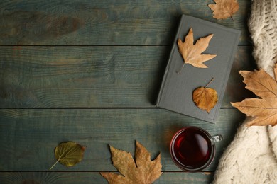 Photo of Cup of tea, book, autumn leaves and sweater on light blue wooden background, flat lay. Space for text