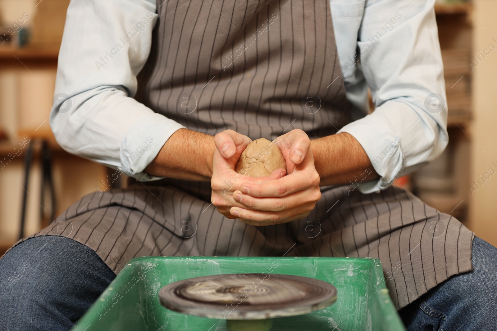 Photo of Man crafting with clay over potter's wheel indoors, closeup