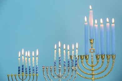 Photo of Hanukkah celebration. Menorahs with burning candles on light blue background, space for text