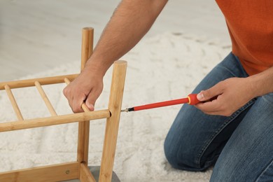 Photo of Man with screwdriver assembling furniture on floor indoors, closeup