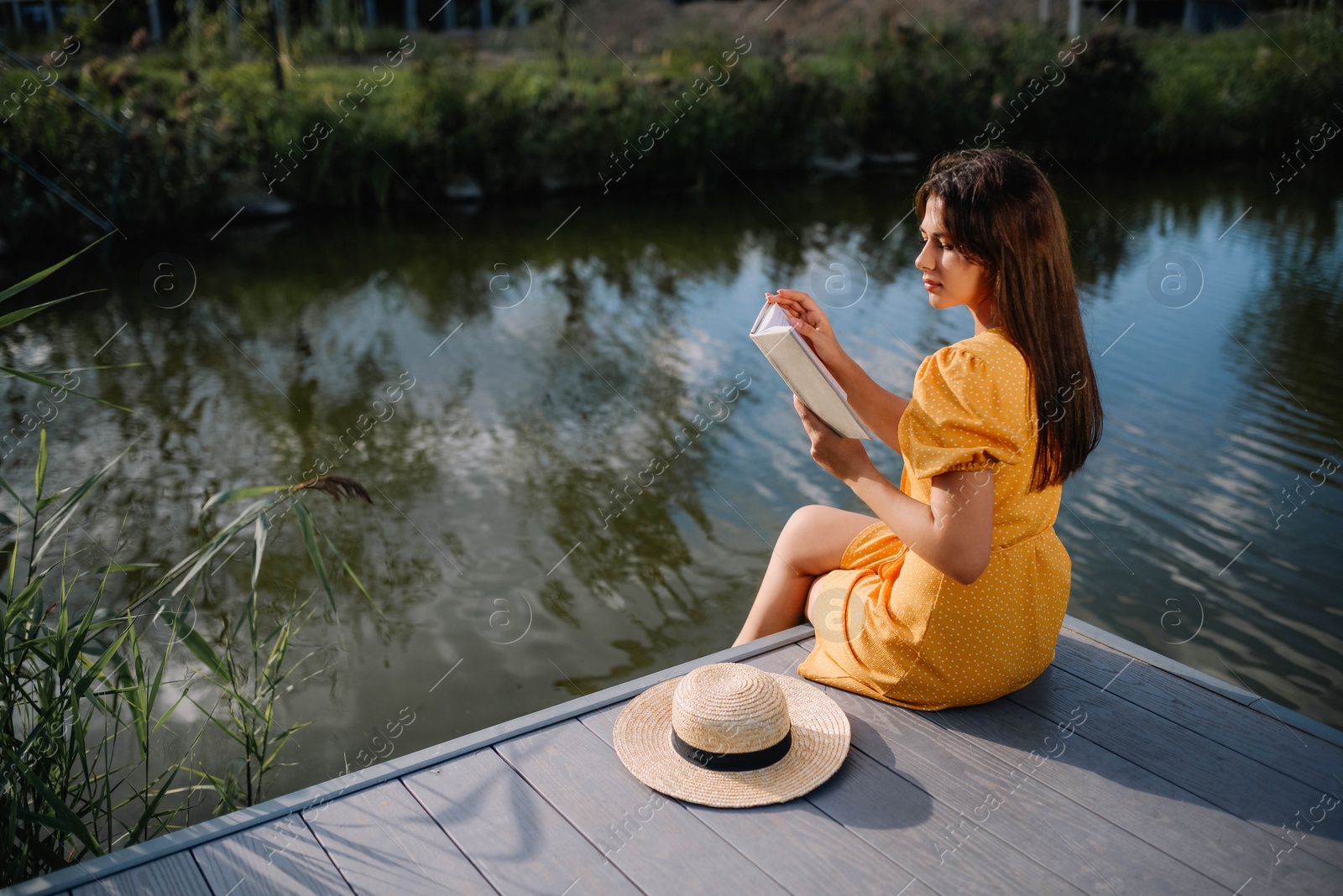 Photo of Young woman reading book near lake on sunny day