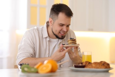 Smiling man with plate of pancakes having tasty breakfast at home