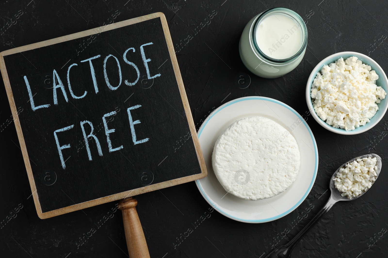 Photo of Dairy products and board with phrase Lactose free on black textured table, flat lay