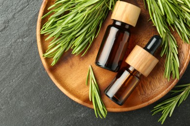 Photo of Essential oils in bottles and rosemary on gray textured table, top view