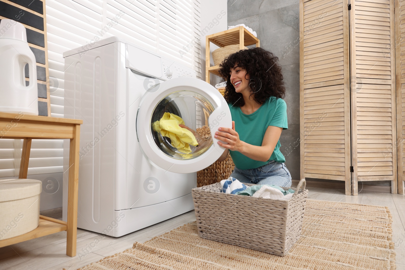 Photo of Happy woman putting laundry into washing machine indoors