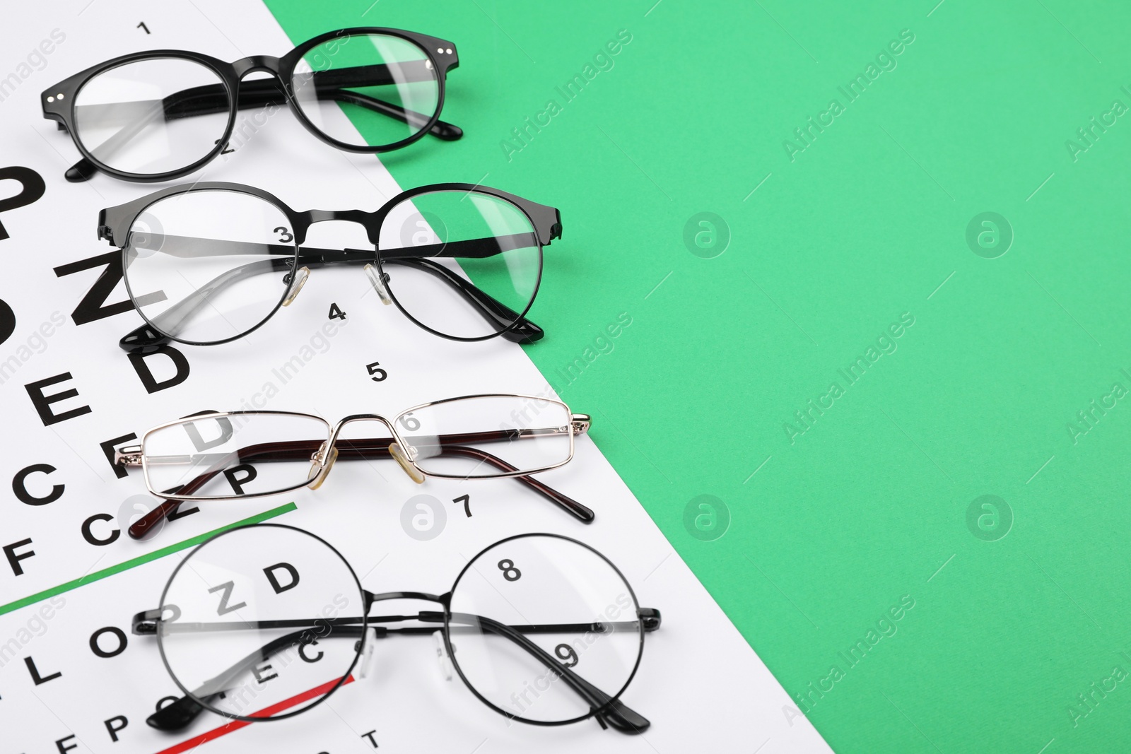 Photo of Vision test chart and glasses on green background, closeup. Space for text