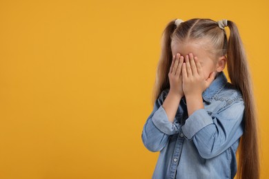 Photo of Resentful girl covering her face with hands on orange background. Space for text