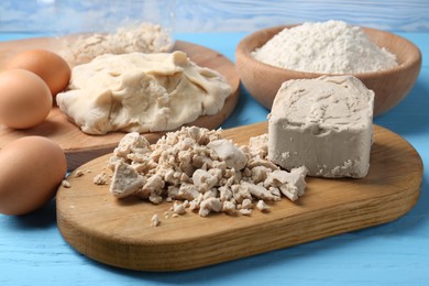 Compressed yeast, eggs, dough and flour on light blue wooden table, closeup