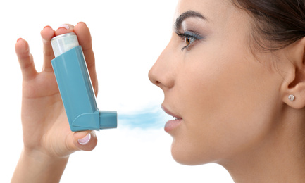 Young woman using asthma inhaler on white background, closeup