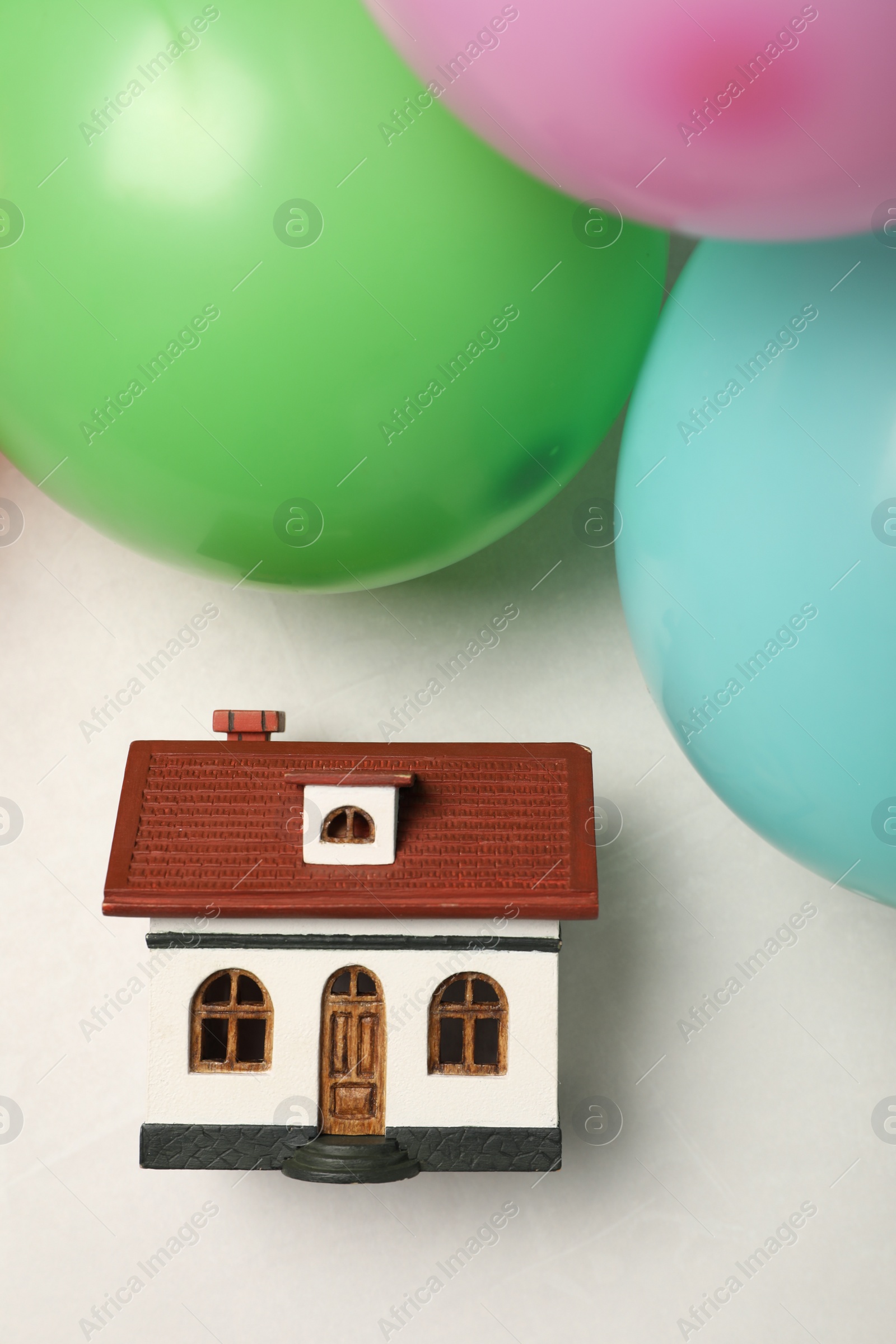 Photo of Wooden house model and balloons on white table, flat lay. Housewarming party