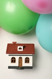 Photo of Wooden house model and balloons on white table, flat lay. Housewarming party