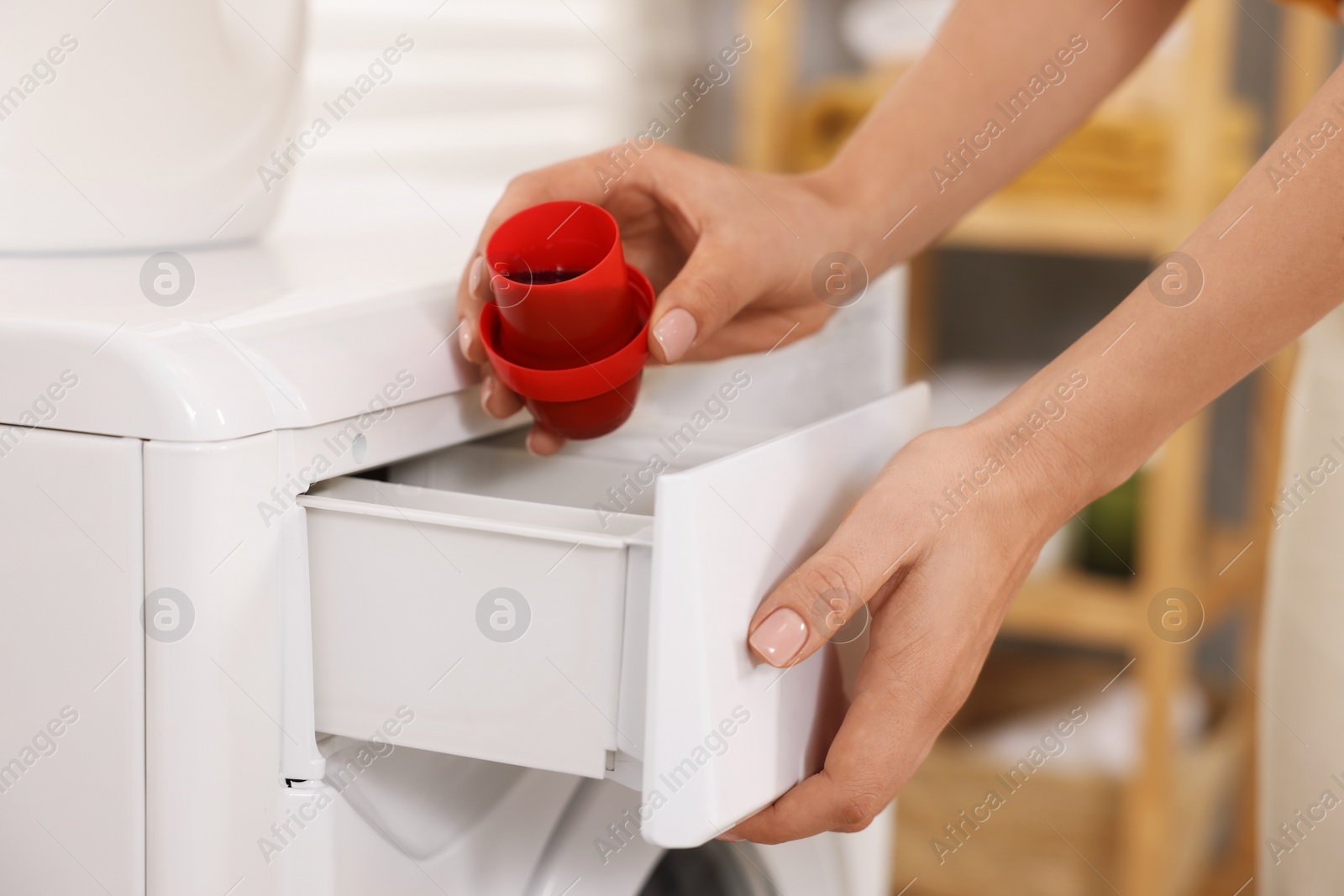Photo of Woman pouring laundry detergent into washing machine indoors, closeup