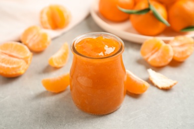 Tasty tangerine jam in glass jar on light grey table