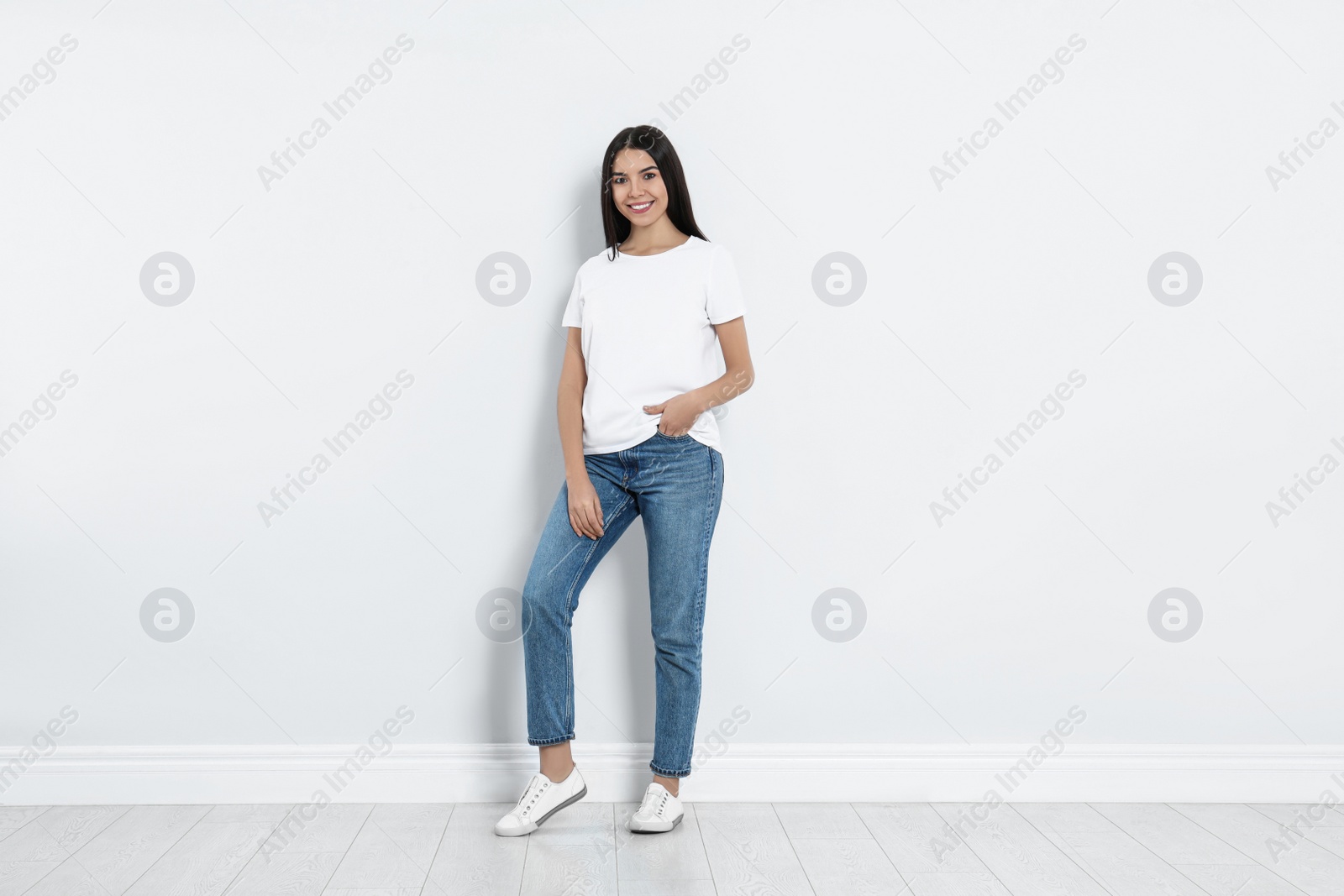 Photo of Young woman in stylish jeans near light wall