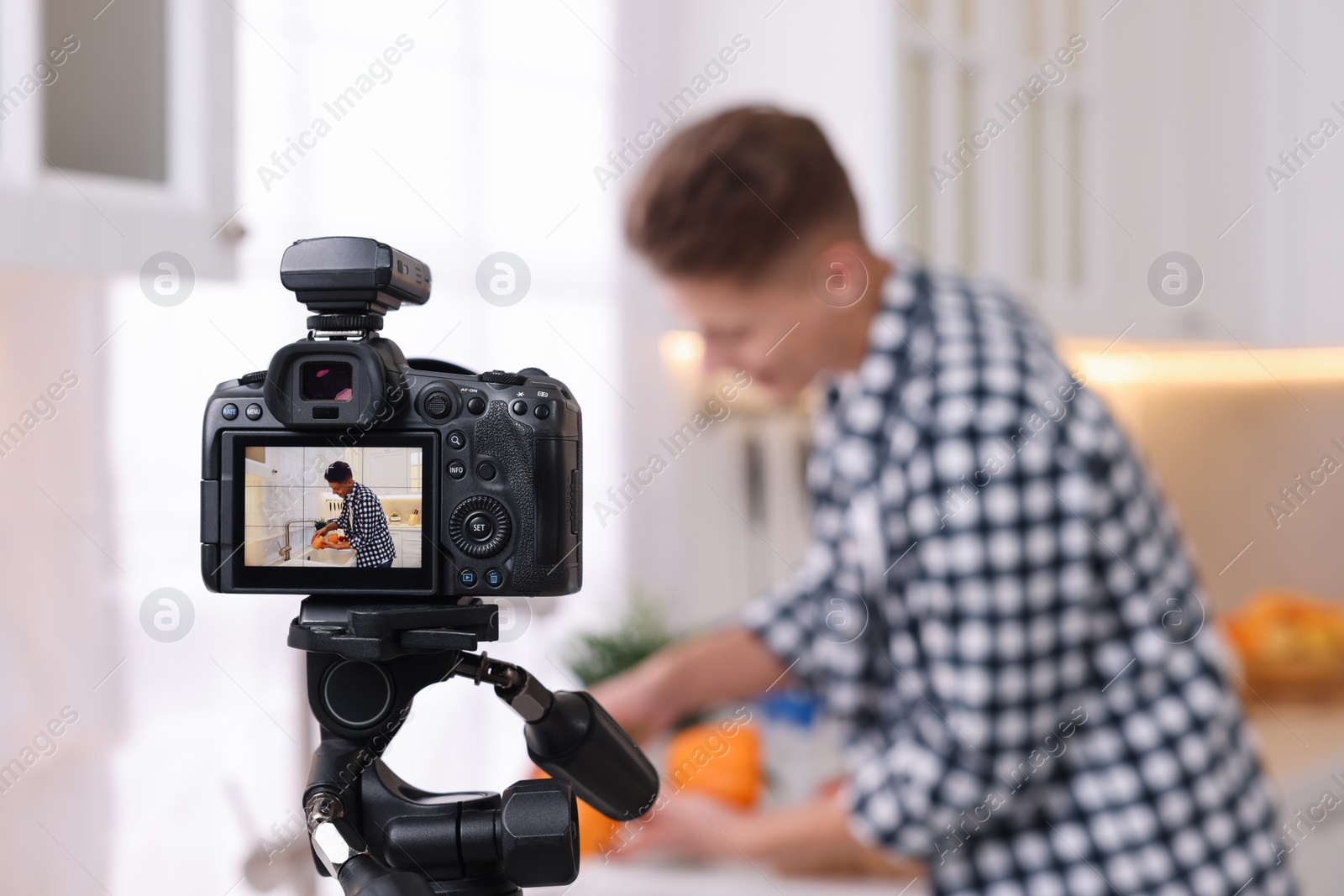 Photo of Food blogger recording video in kitchen, focus on camera