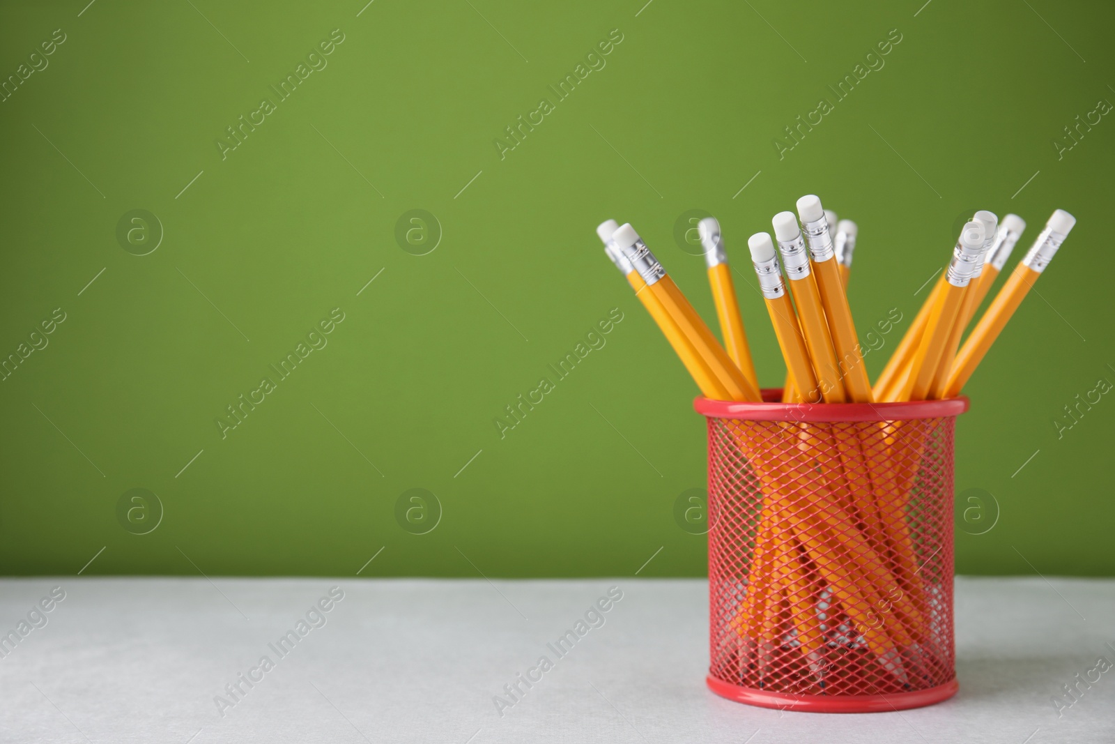 Photo of Many sharp pencils in holder on light table against green background, space for text